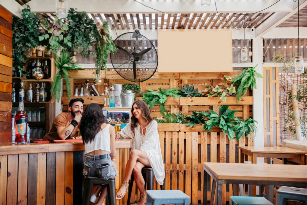 Três amigos se divertem em um bar com decoração sustentável e cardápio moderno, exemplo de como práticas conscientes podem inspirar o setor: o que é ESG no foodservice aplicado à experiência do cliente.