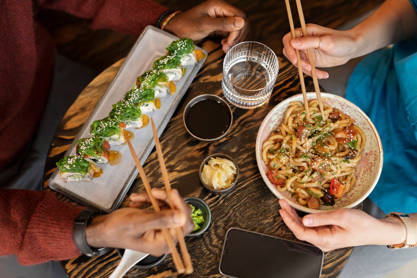 Pessoas desfrutando de pratos típicos da culinária japonesa em restaurante. Exemplo prático de apresentação de pratos que pode inspirar quem busca como criar cardápio de restaurante japonês.
