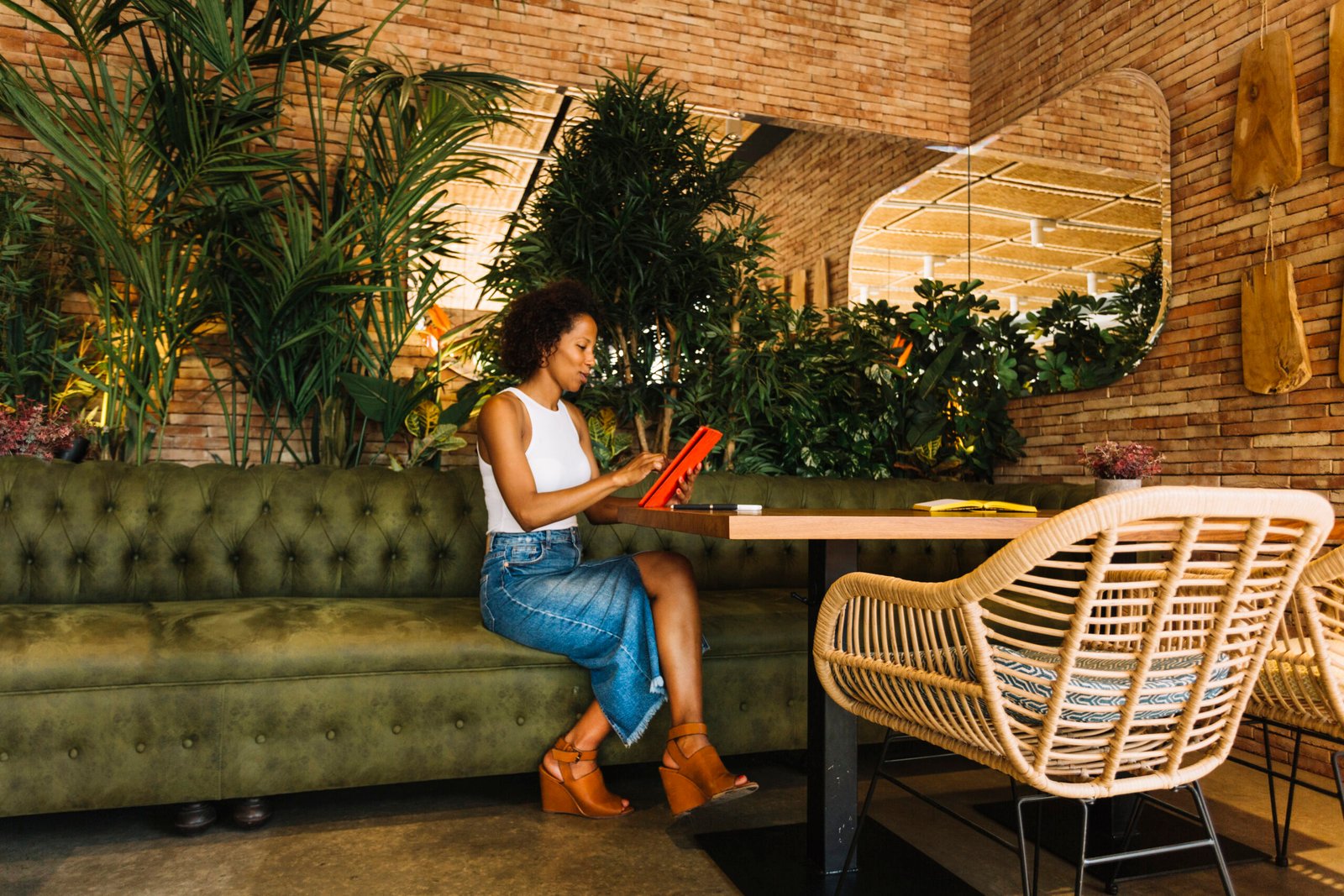 Mulher sentada em um restaurante moderno e aconchegante, usando um tablet à mesa em um ambiente com plantas, madeira e design contemporâneo que representa tendências de restaurante focadas em experiência, tecnologia e conforto.