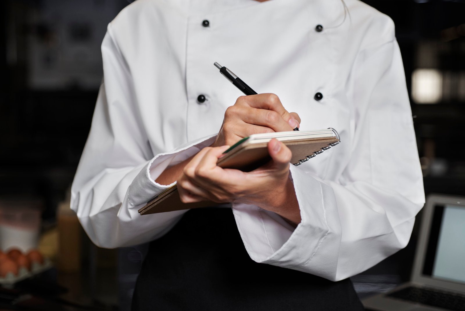 Chef anotando informações em um caderno na cozinha, representando um checklist para restaurante no planejamento de operações.