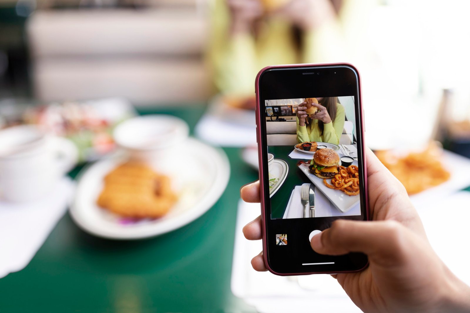 Pessoa fotografando um hambúrguer com o celular em um restaurante, ilustrando como fotos de comida ajudam restaurantes a atrair clientes no Instagram.