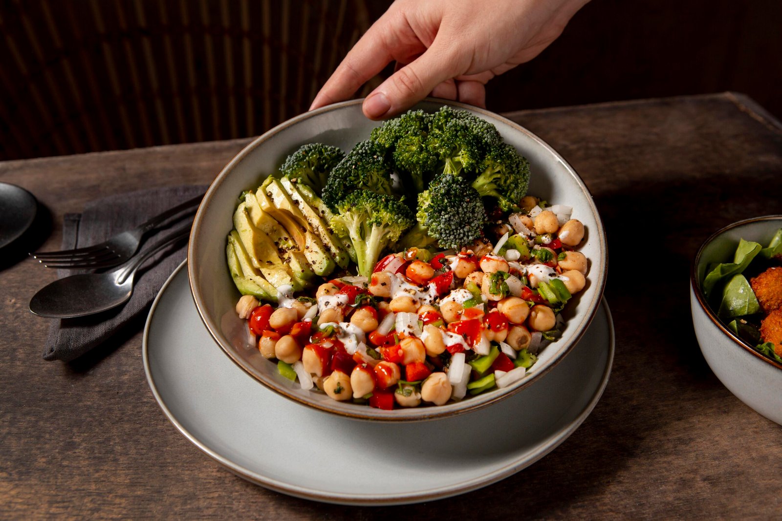 Cardápio inclusivo com bowl saudável de grão-de-bico, brócolis, abacate e legumes frescos servido em prato sobre mesa de madeira.